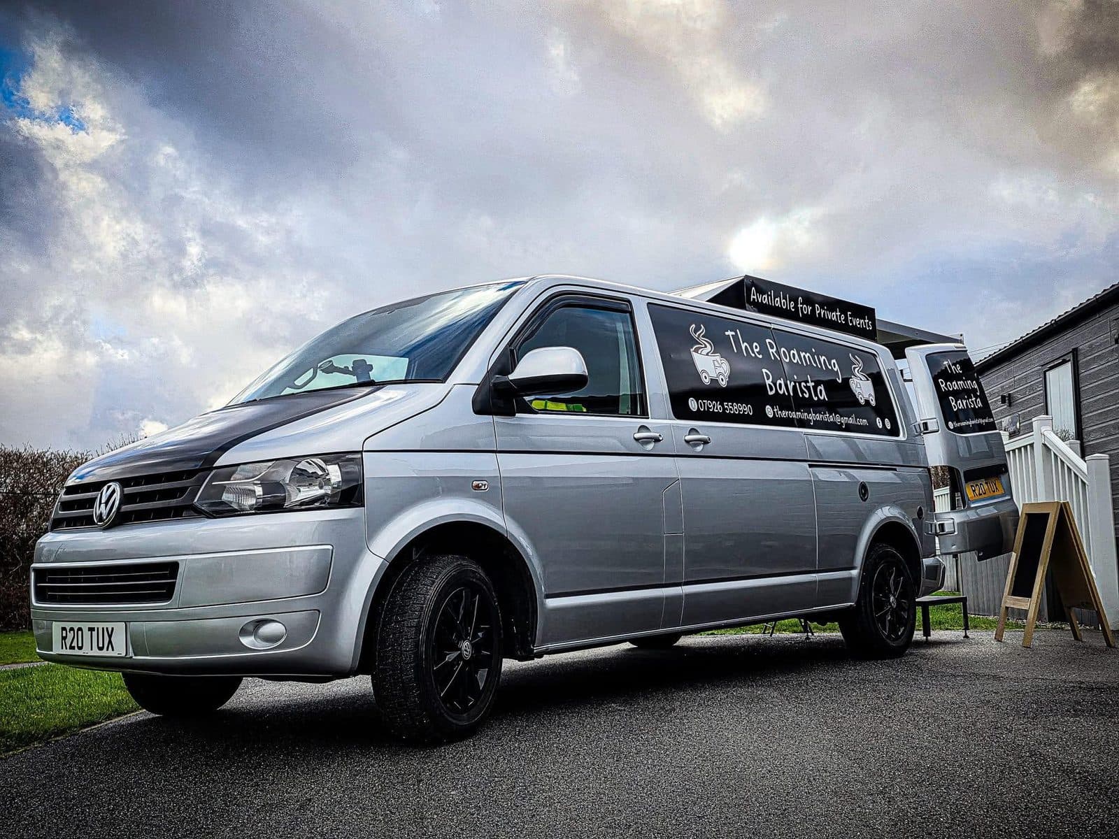 The Roaming Barista's silver Volkswagen Transporter van with tuxedo-black livery and a deployed white gazebo at a Cornish event